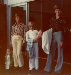 Three people standing in front of a building, two of them holding a baby.