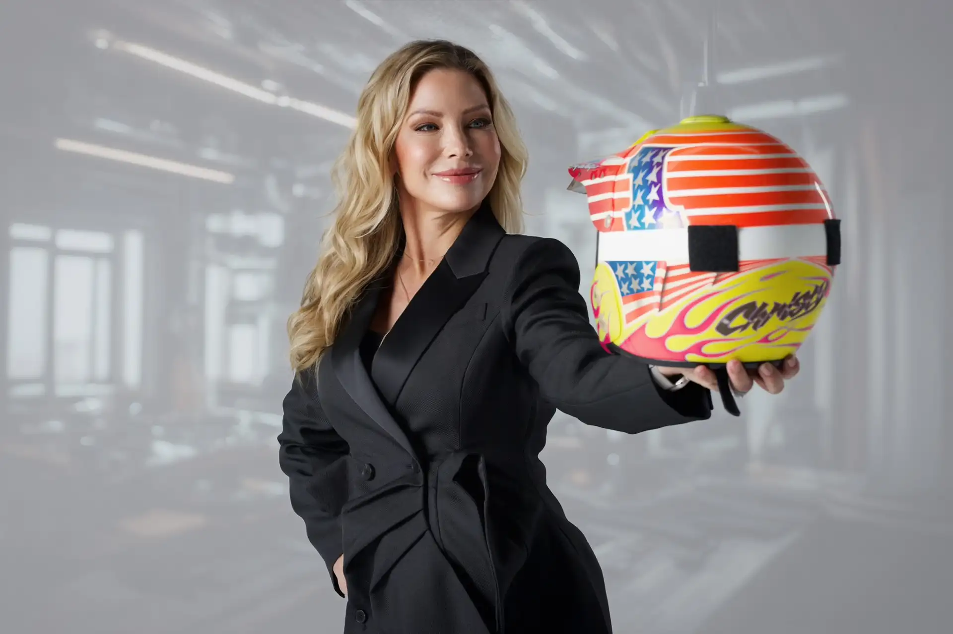 Christy Swaid in a dark blazer holding a racing helmet with an American flag design