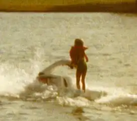 A woman in a life jacket is riding a jet ski on a lake.